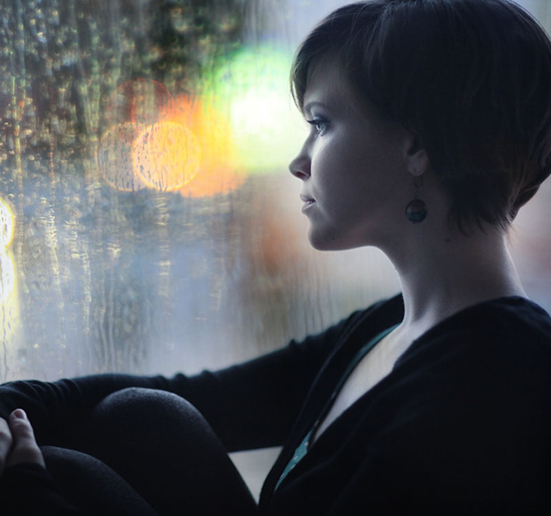 sad girl on the windowsill looking out the window